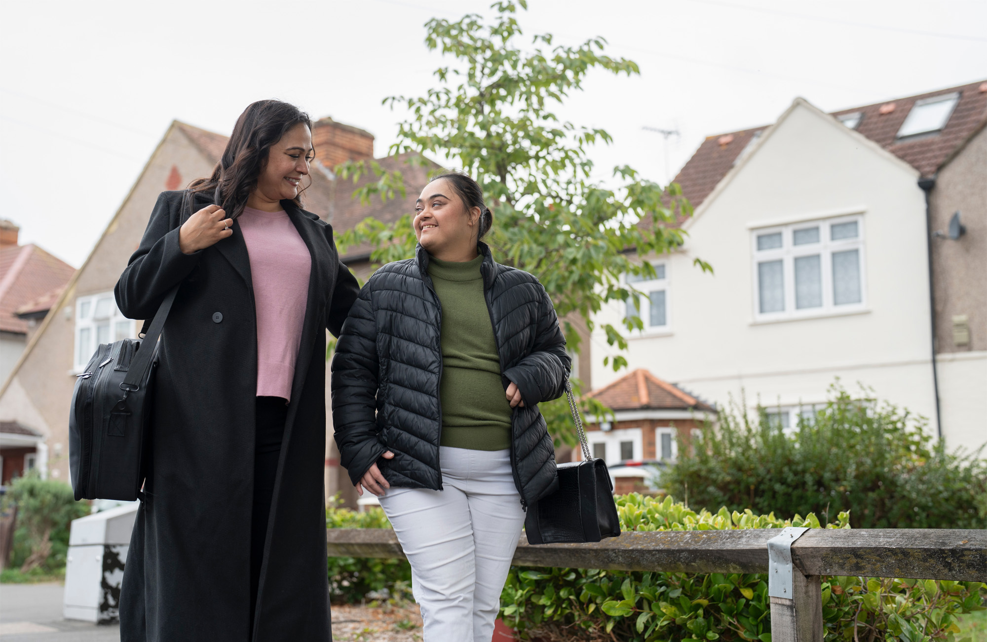 Two people walking side-by-side with houses behind them.