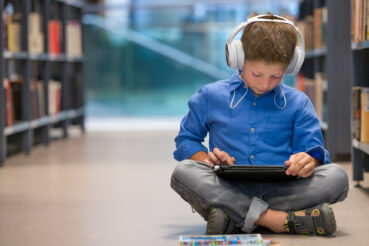 boy in library using assistive technology (headphones and tablet) to learn