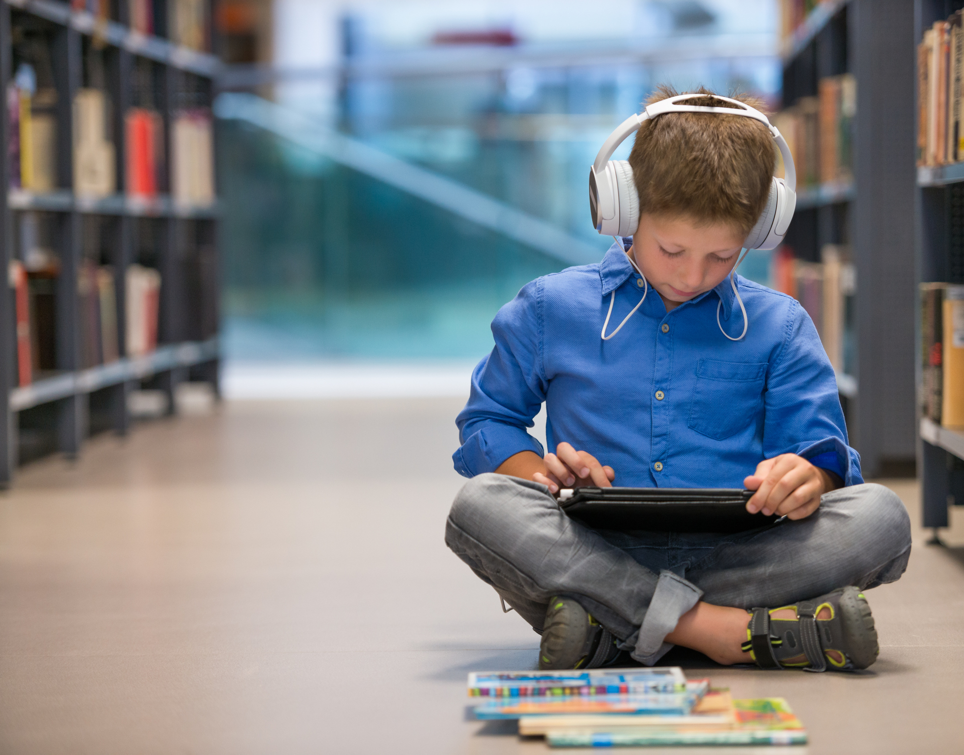 boy in library using assistive technology (headphones and tablet) to learn