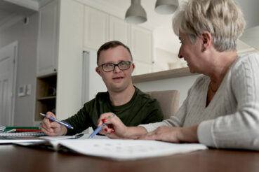 Two individuals sitting at a table looking at one another with papers in front of them.