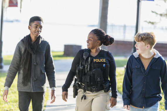 police officer walks down street with teenagers conversing