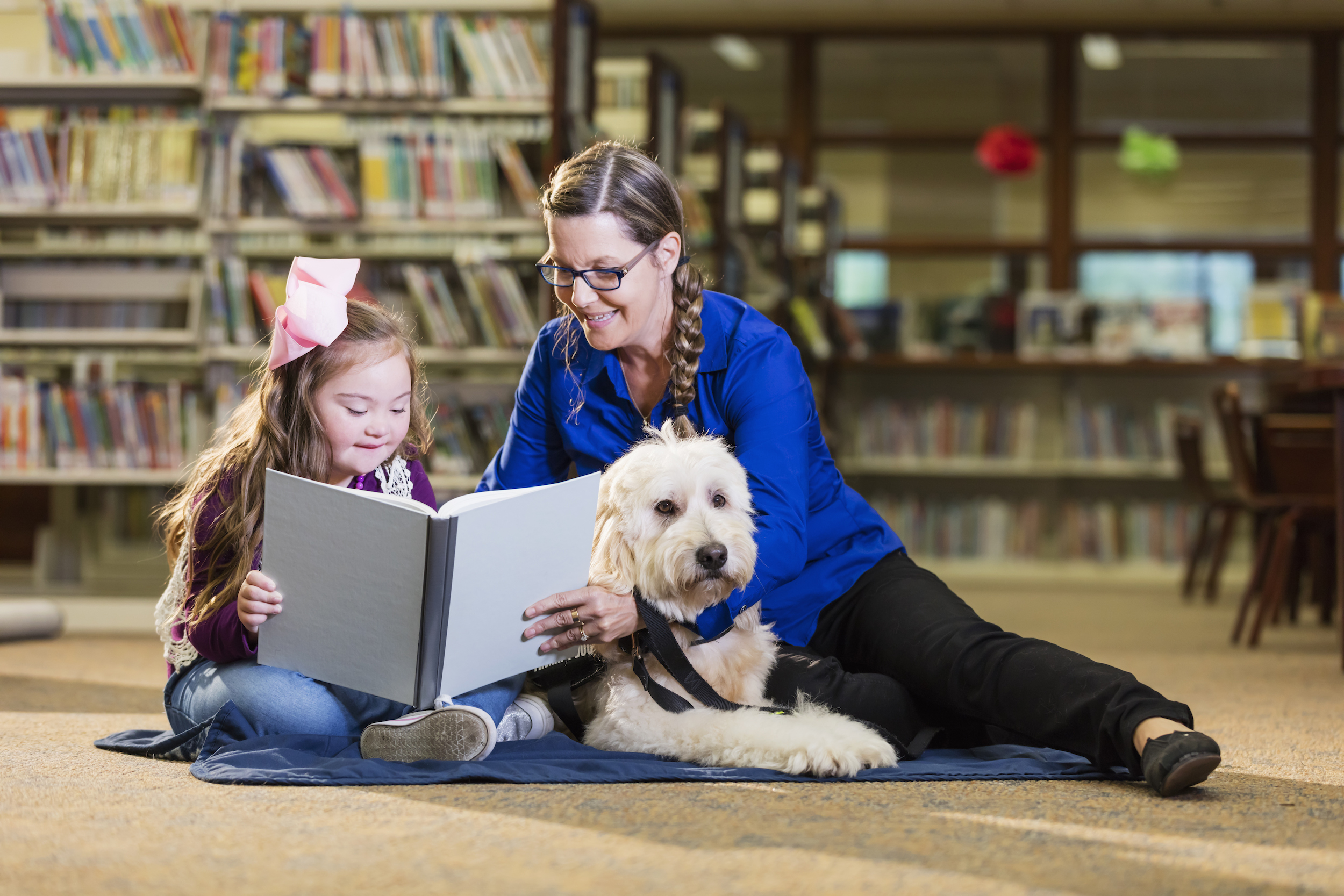 Special needs student reading with an assistant and a therapy dog